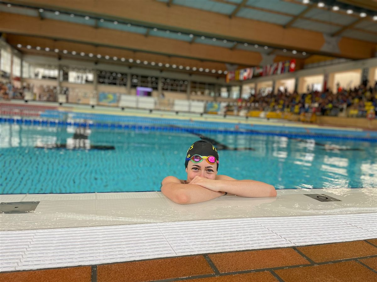 Zoë leaning on the edge of an indoor pool decorated with national flags