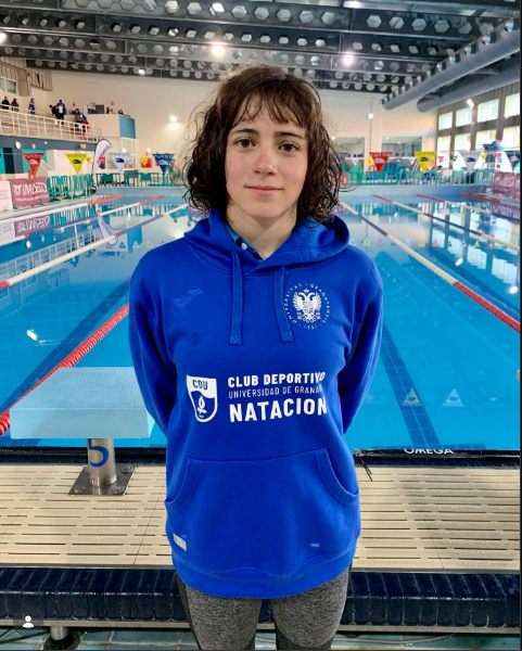 Zoë in a University of Granada hoodie in front of a competition pool