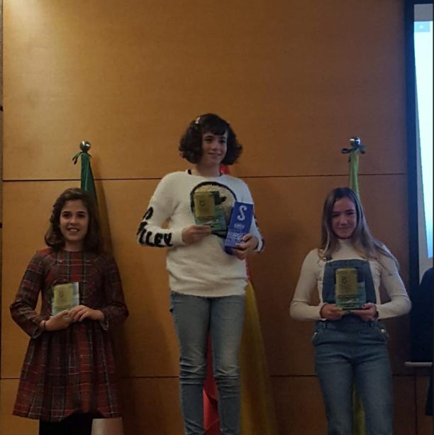 Zoë on the top step of the podium holding two trophies at an awards ceremony