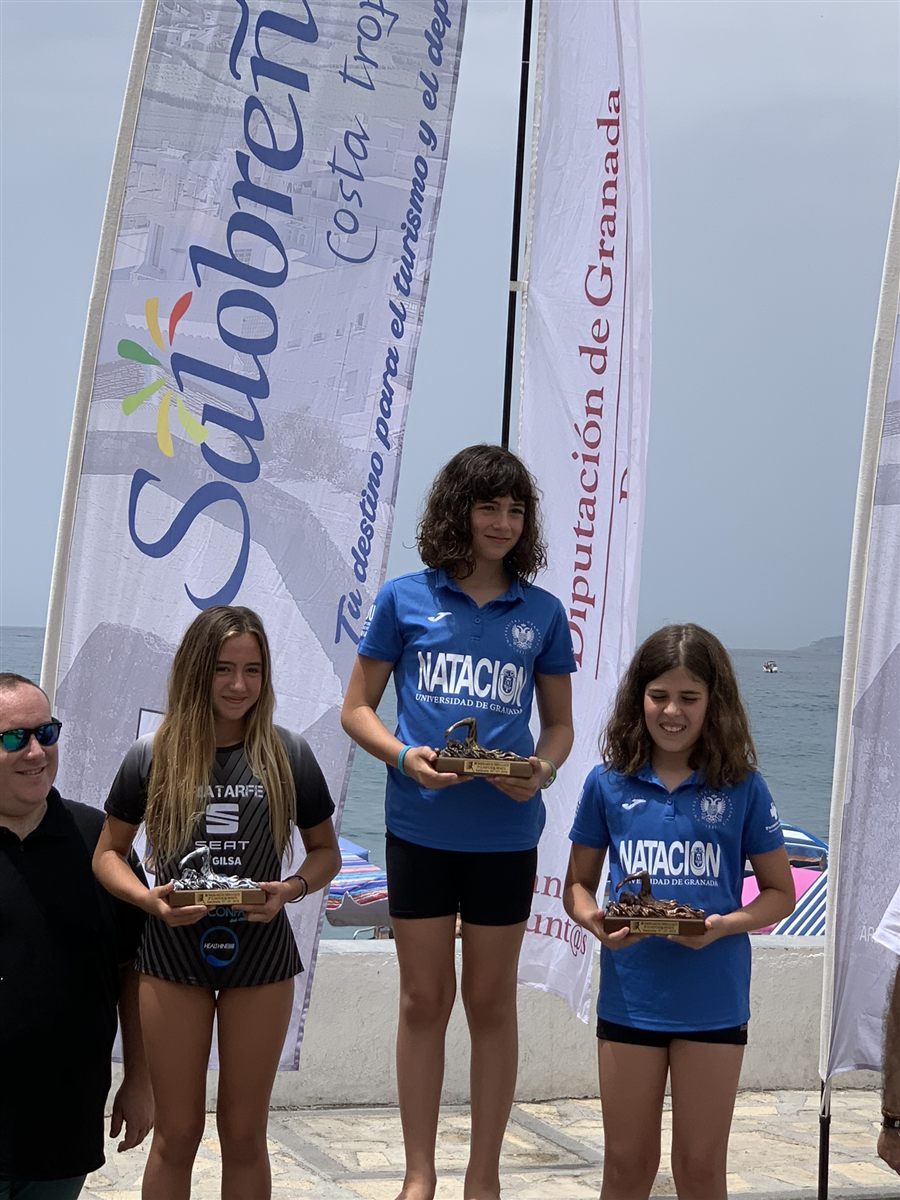 Zoë on the podium with a trophy at an open-water race on the beach in Salobreña