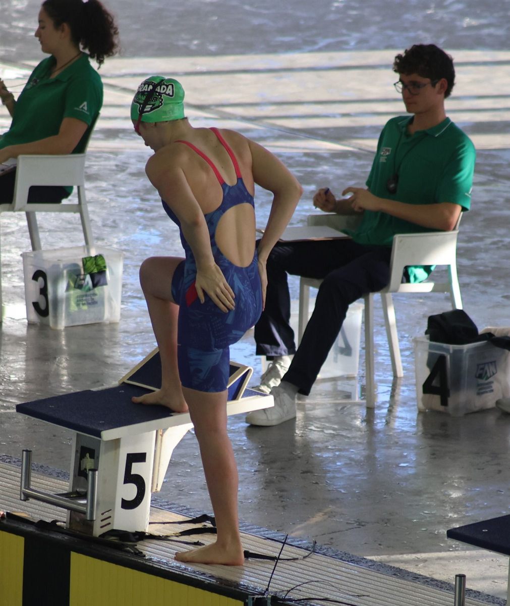 Zoë stepping onto the lane 5 starting block in a club cap