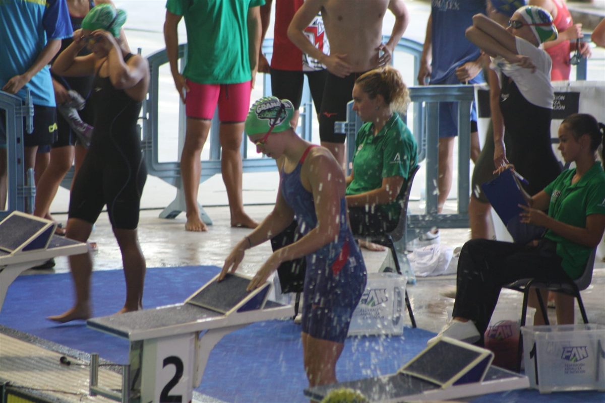 Swimmers in green caps in the start area of an Andalusian championship